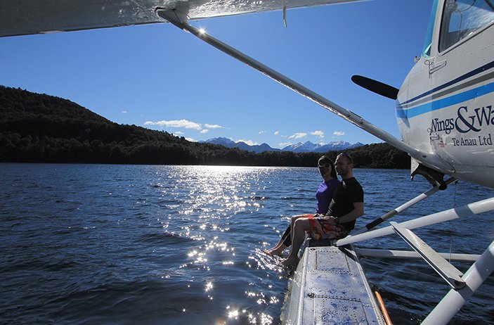 Two people sitting on the float of a sea plane on Lake Te Anau enjoying the views